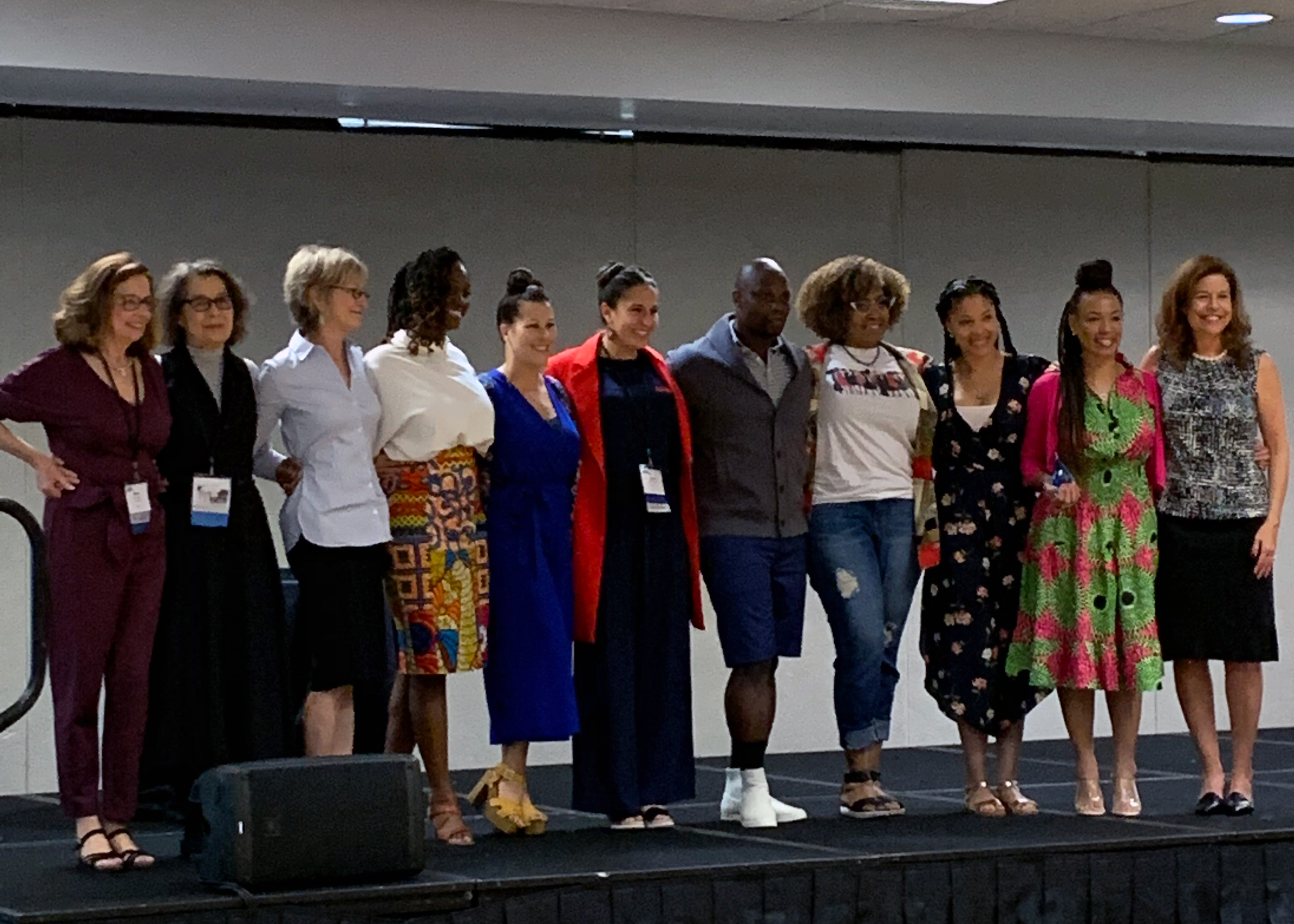 A group of women up on a stage standing in a line and posing for a photo