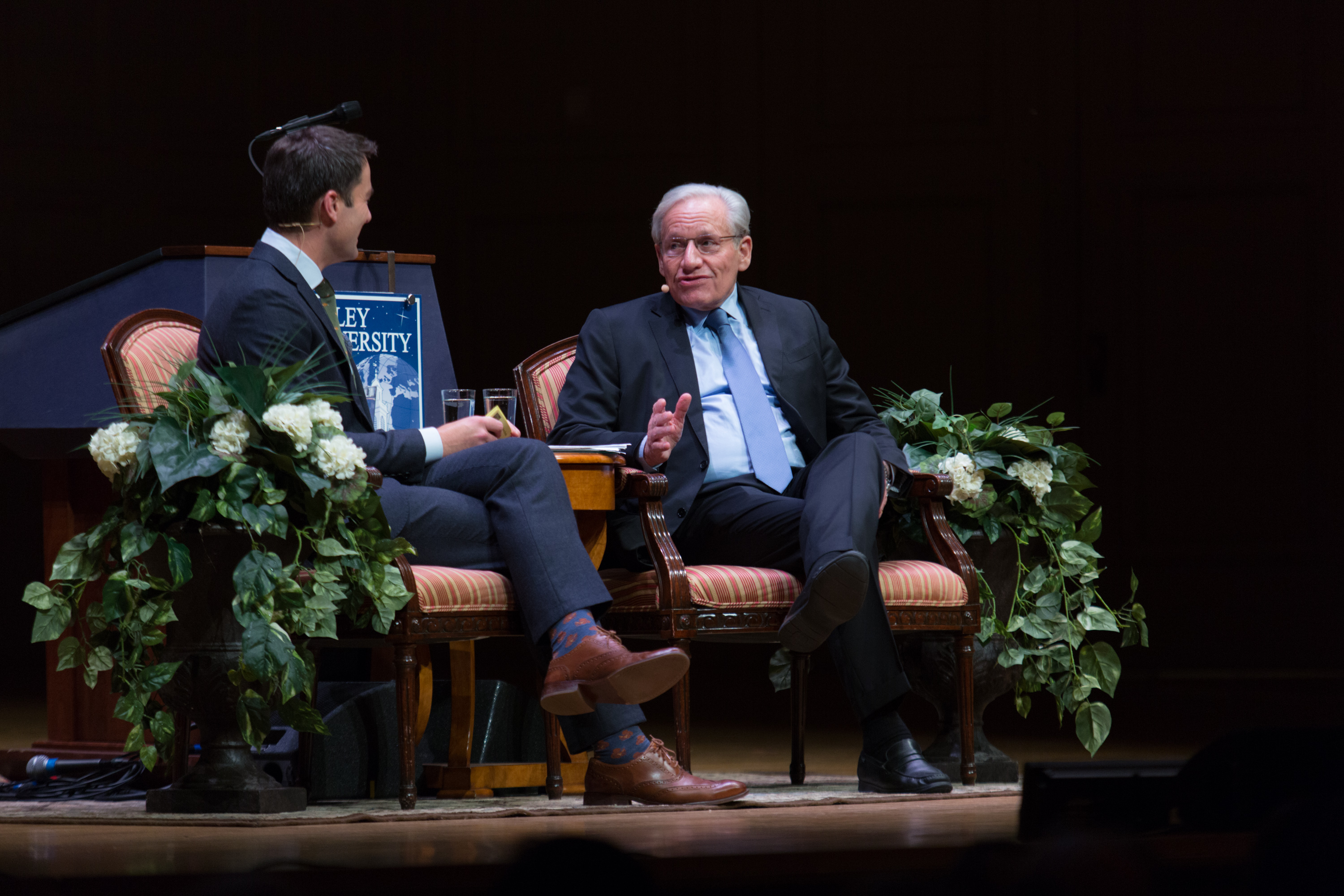 two men sitting on a stage in conversation for an interview