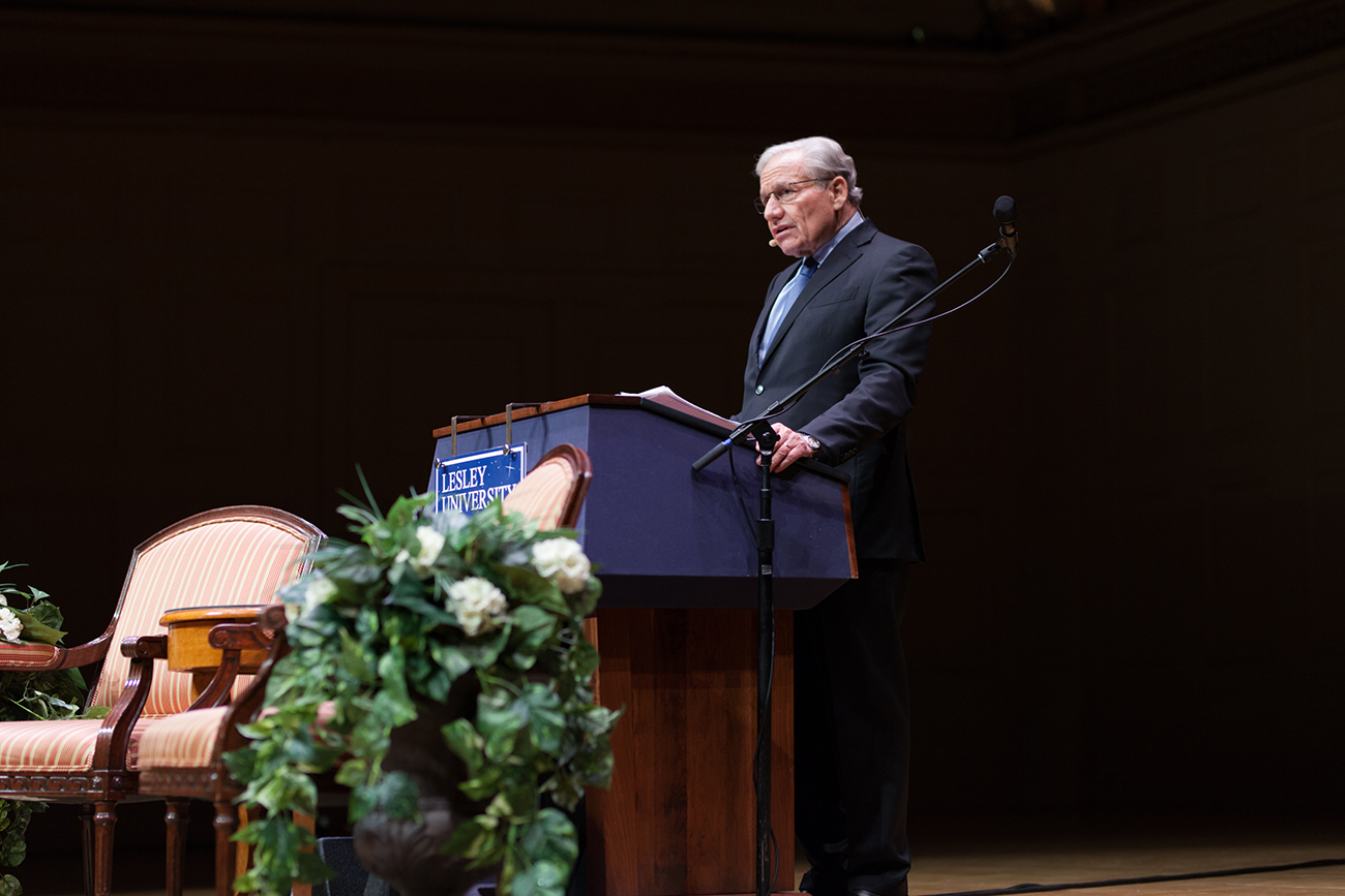 Man in a suit standing behind a podium giving a speech on a stage.