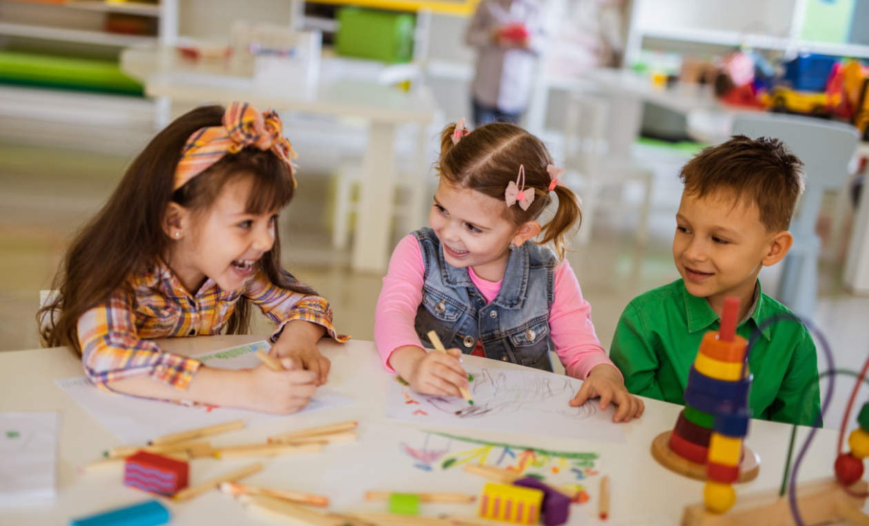 Three children smile and write together at a table.