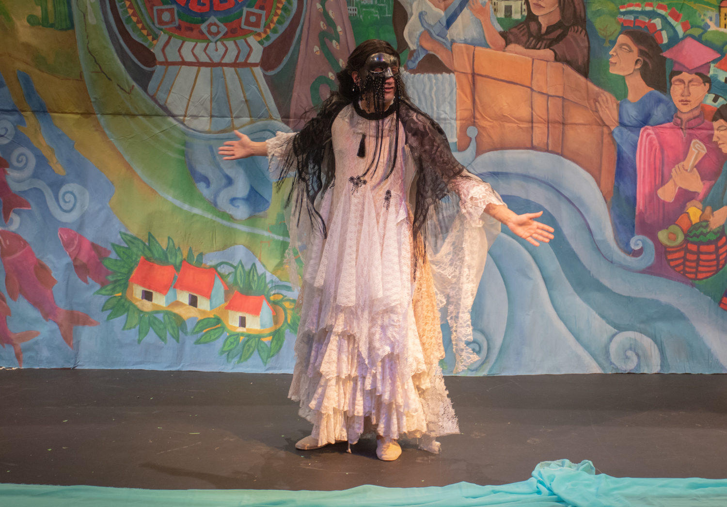 An actor in a black mask wearing a long, white lace dress.