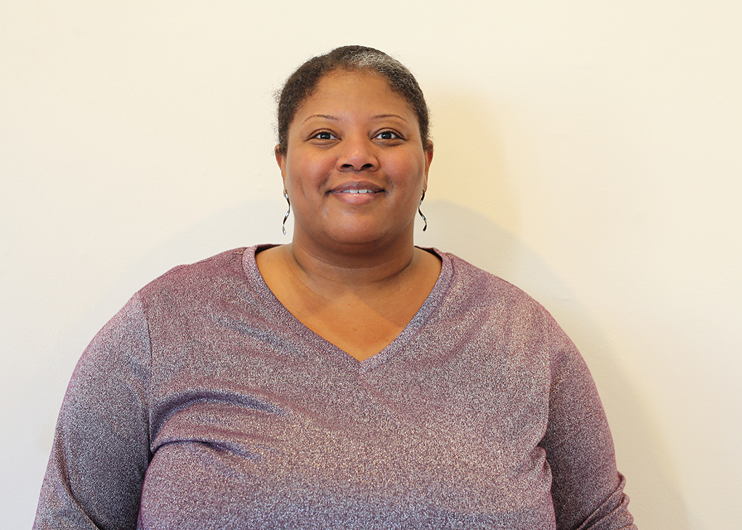 Kenisha Coy in a purple shirt standing in front of a white wall