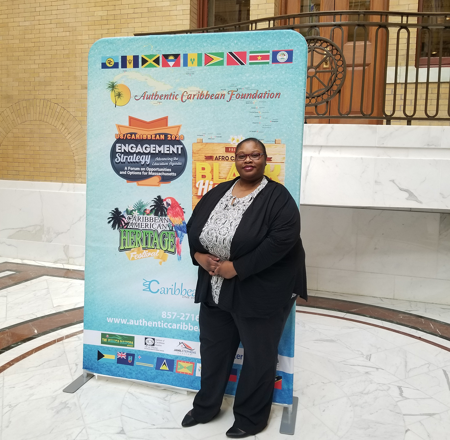 Professor Michelle Vital poses in front of a banner on the State House steps