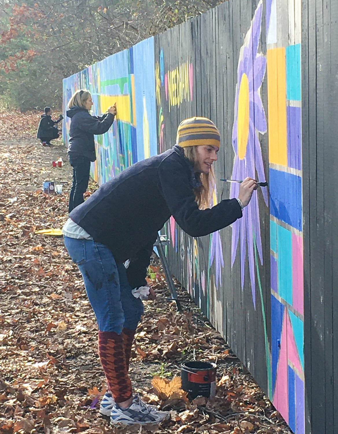 People paint a mural on a fence