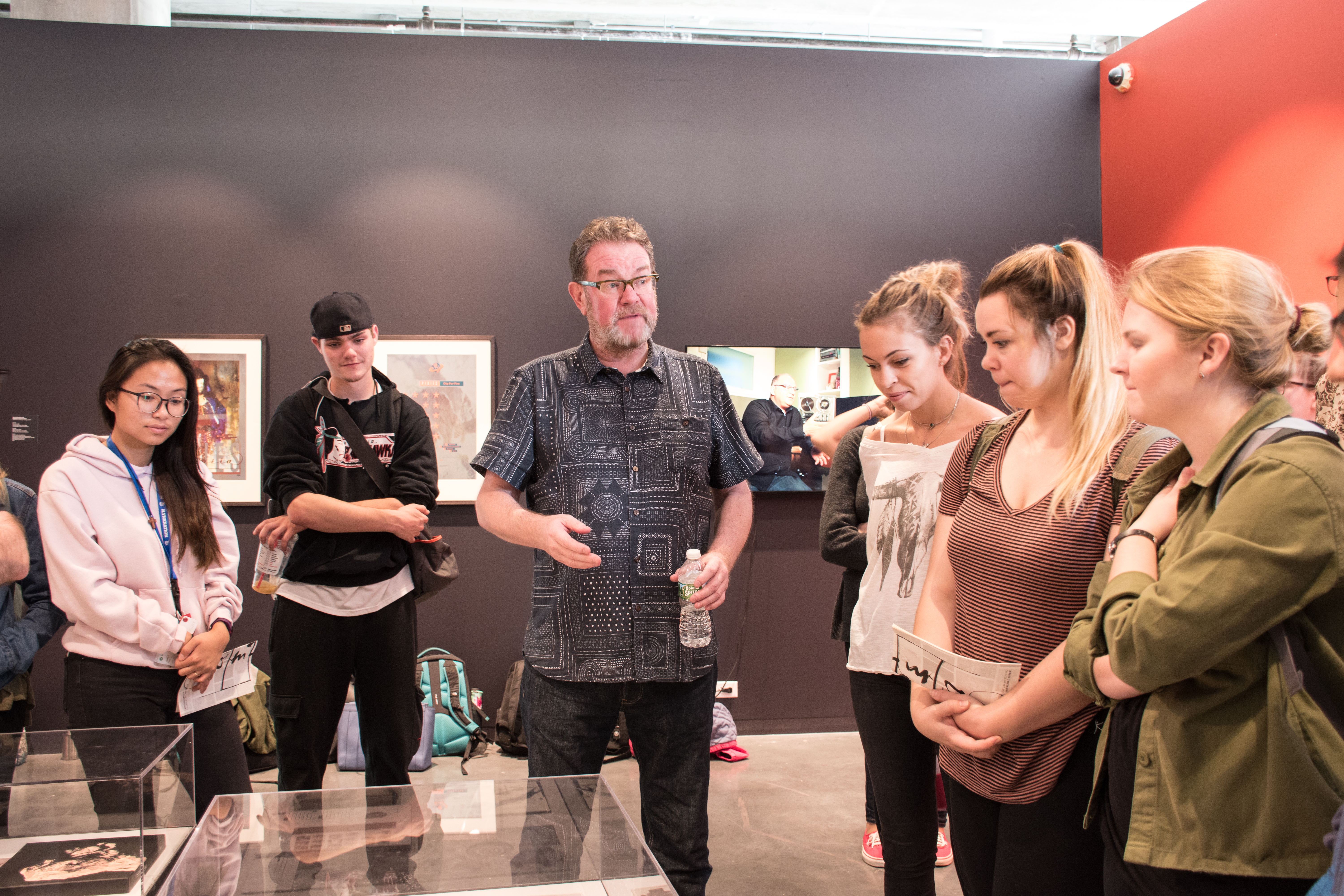 Vaughan Oliver stands in the middle of a group of design students in the art gallery.