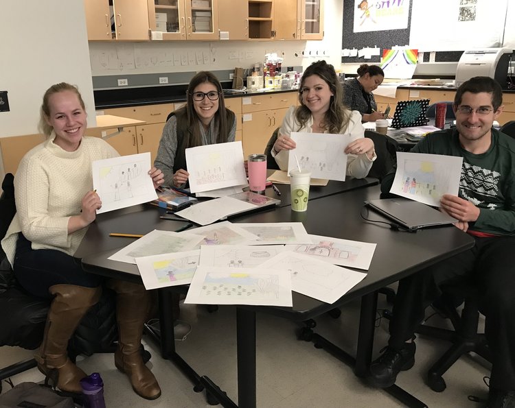 Lesley students in a classroom at University Hall showing their illustrations from children's books.