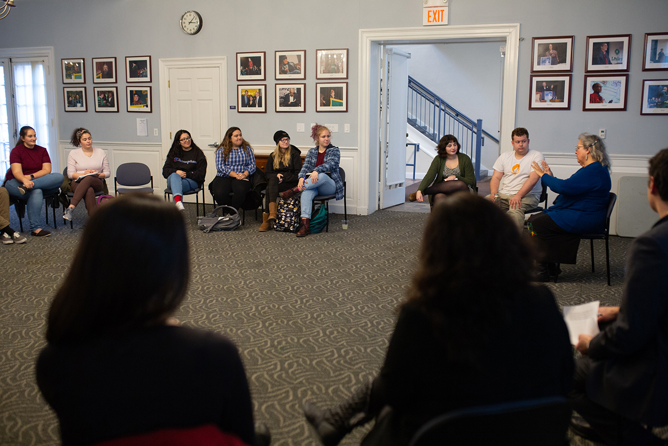 A group of students seated in Alumni Hall in a circle listening to a lecture