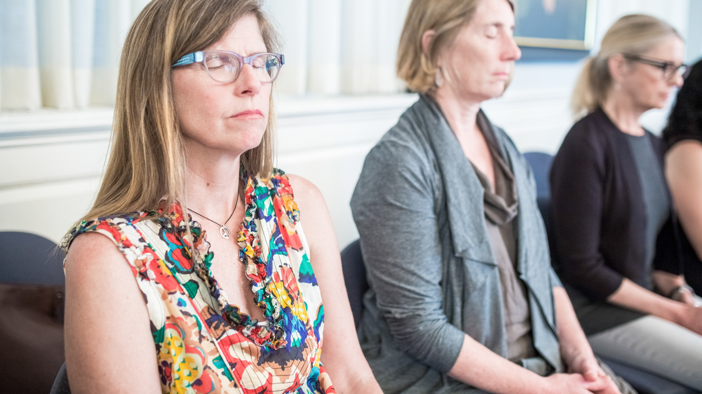 Three students sit quietly in meditation with their eyes closed.