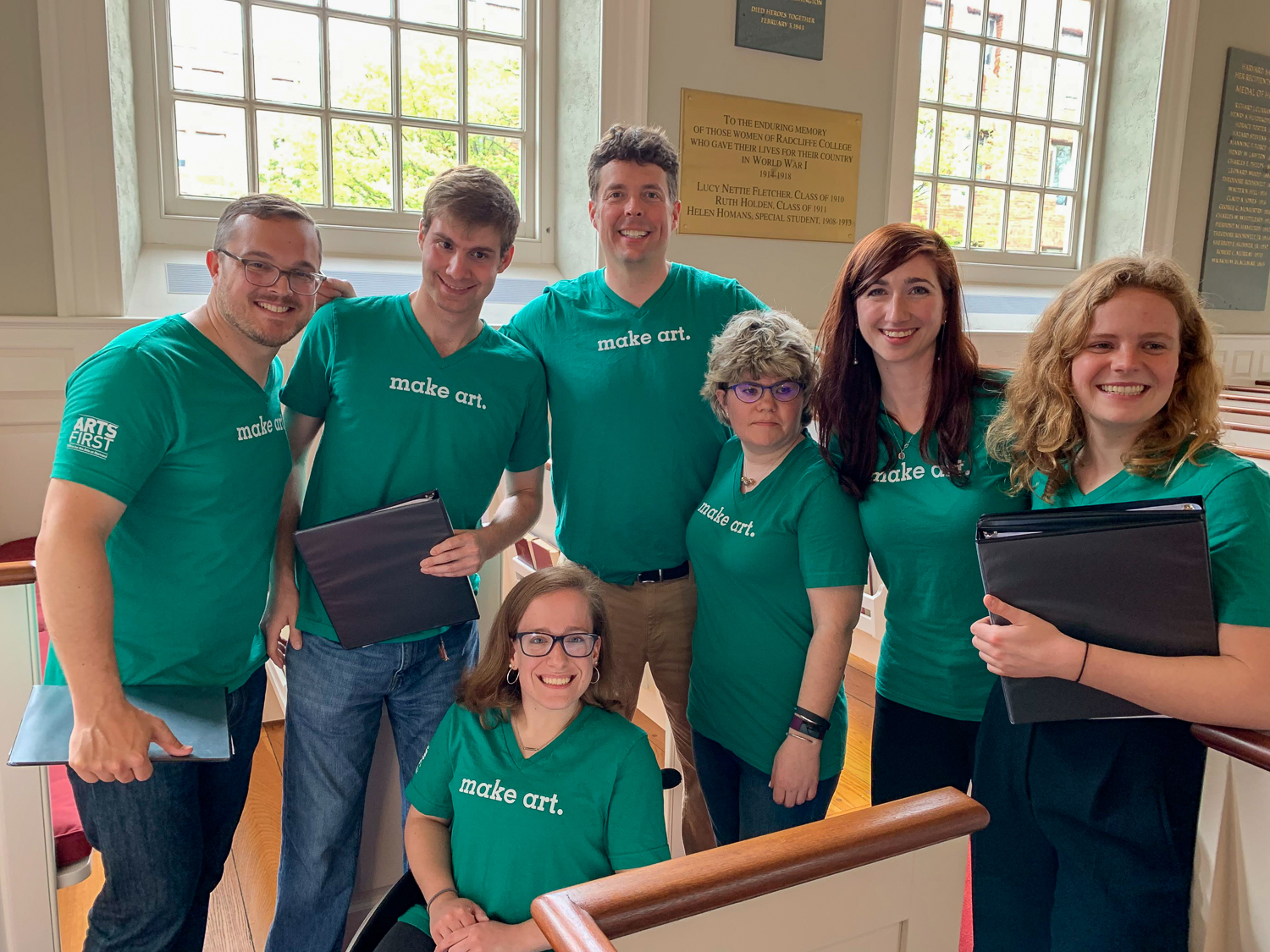 Group of people sitting in or standing around pews wearing green shirts that say "Make Art"