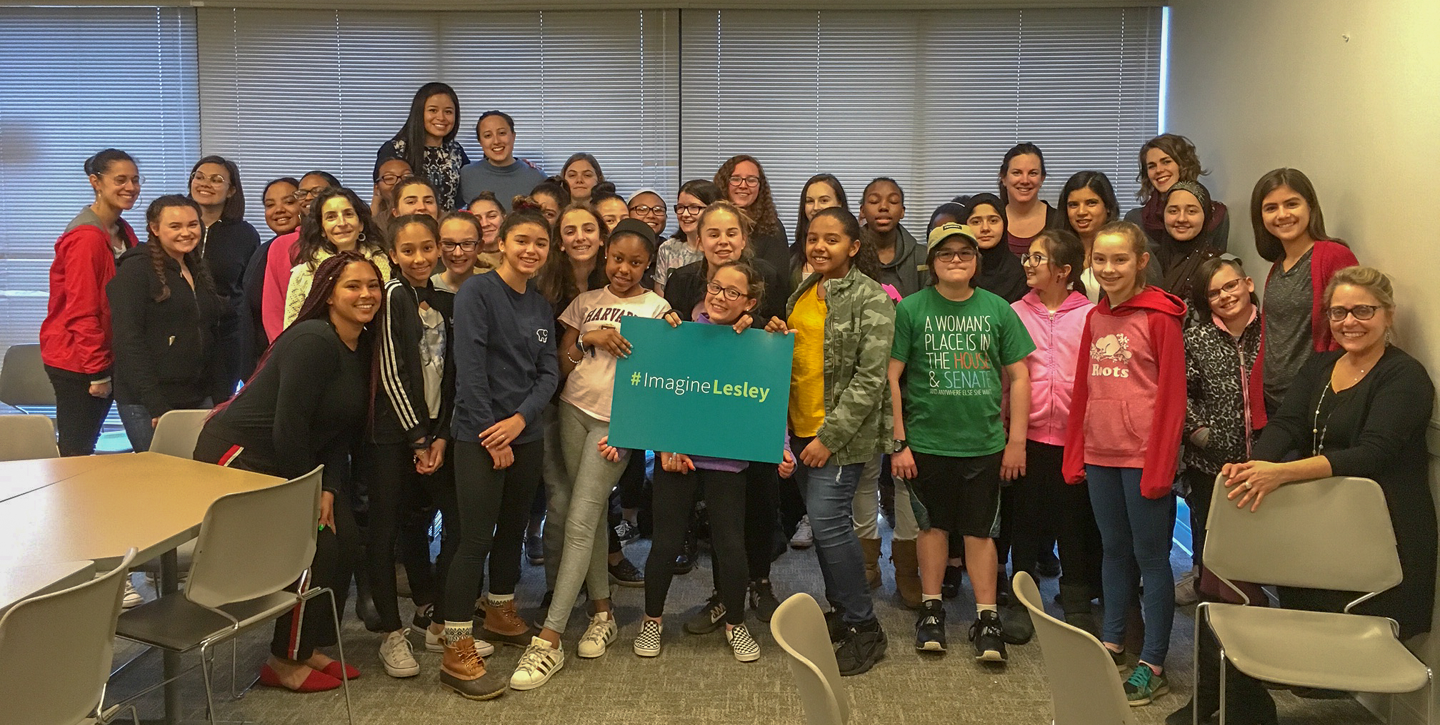 Group shot of teenage girls with one holding the green #ImagineLesley sign in the center.