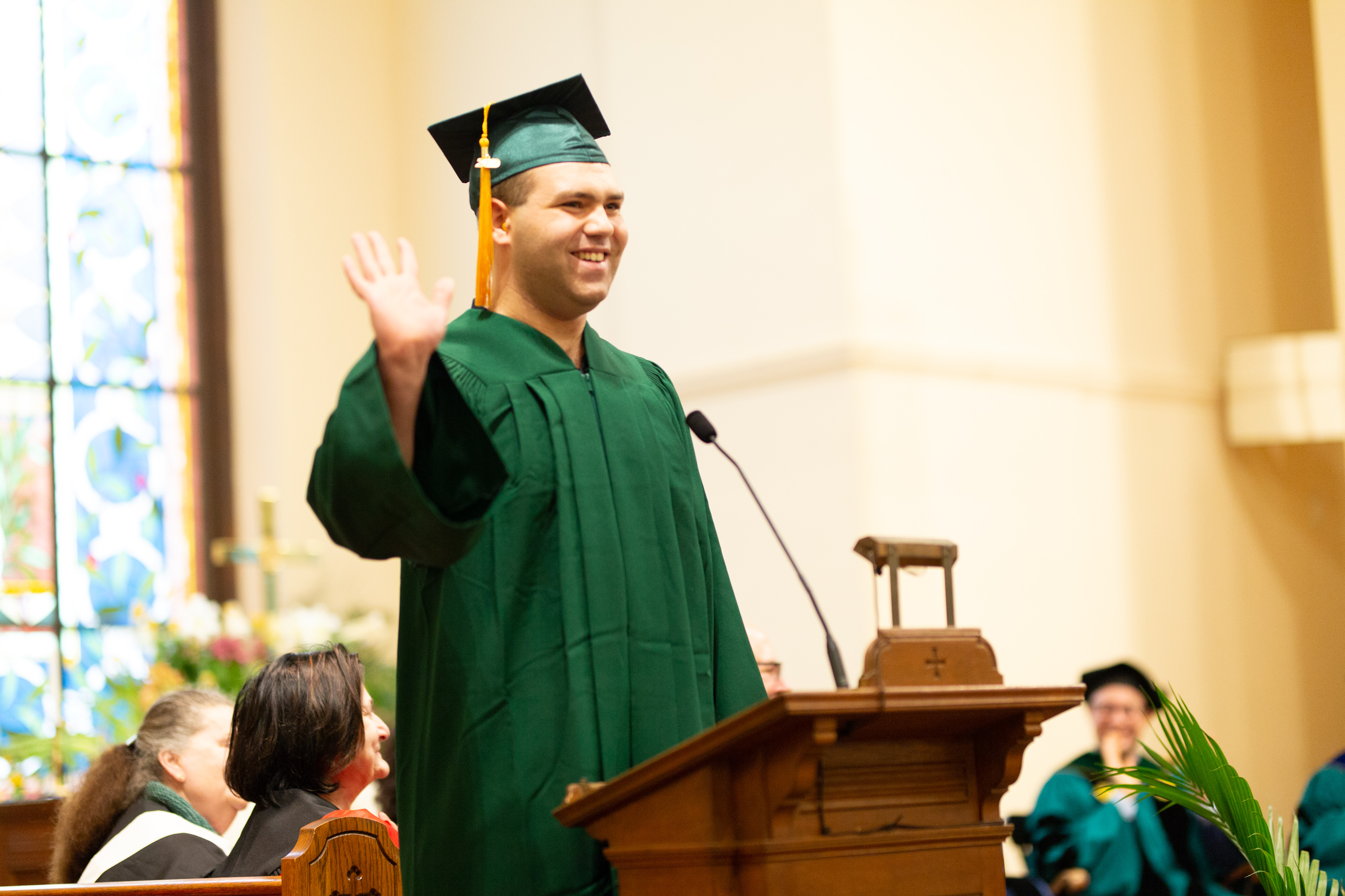 Student speaker waves from the podium in cap and gown