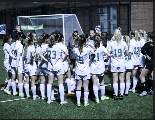 Women's soccer on the field gathered together listening to their coach.