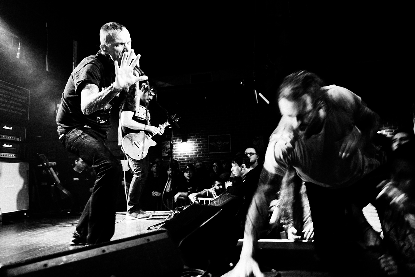 black and white photo of live concert with lead singer performing and audience member climbing on stage.