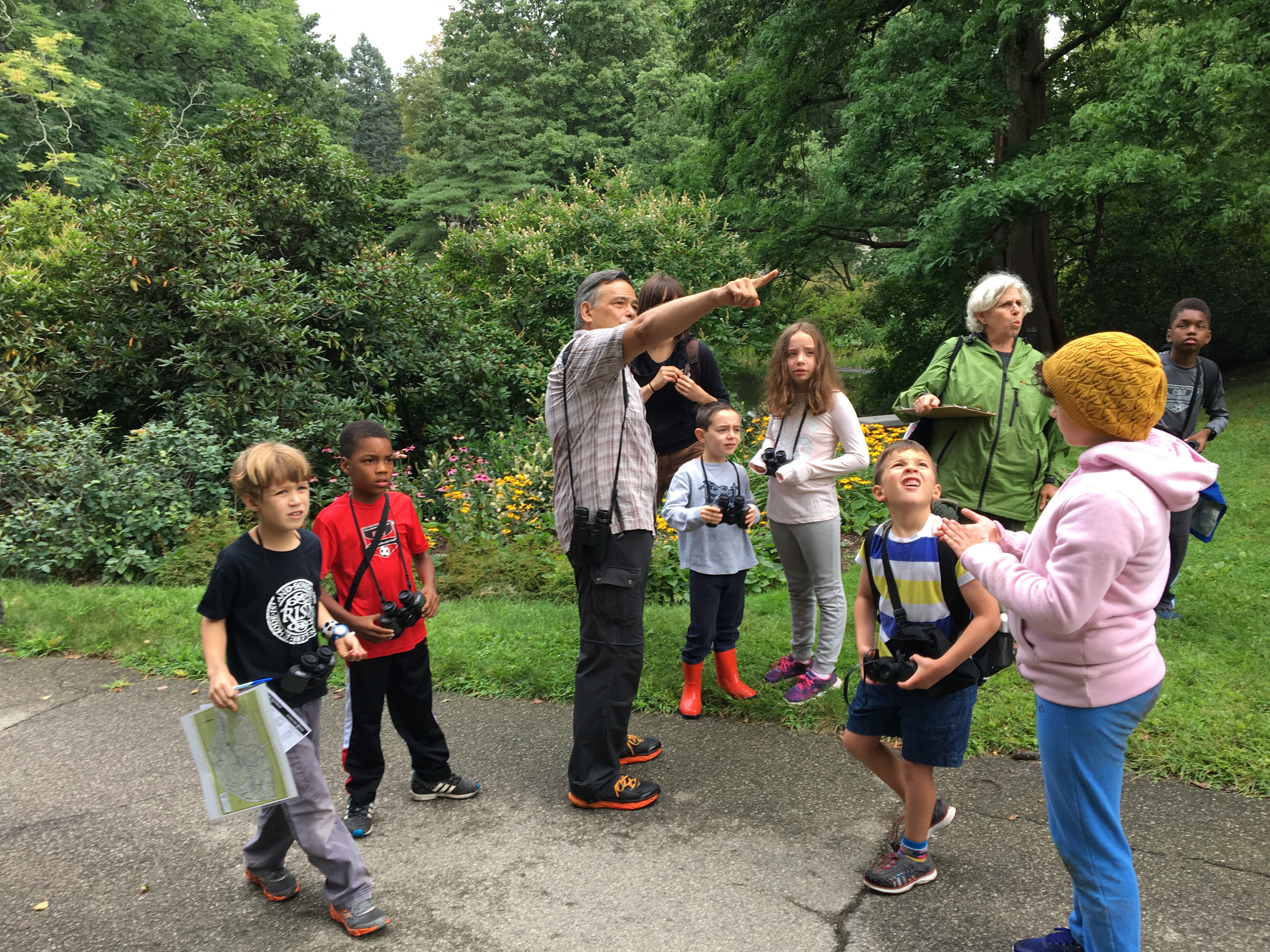 Mt Auburn Morimoto Rauchwerk students exploring outdoors with cameras. Group leader is pointing at something and everyone is looking