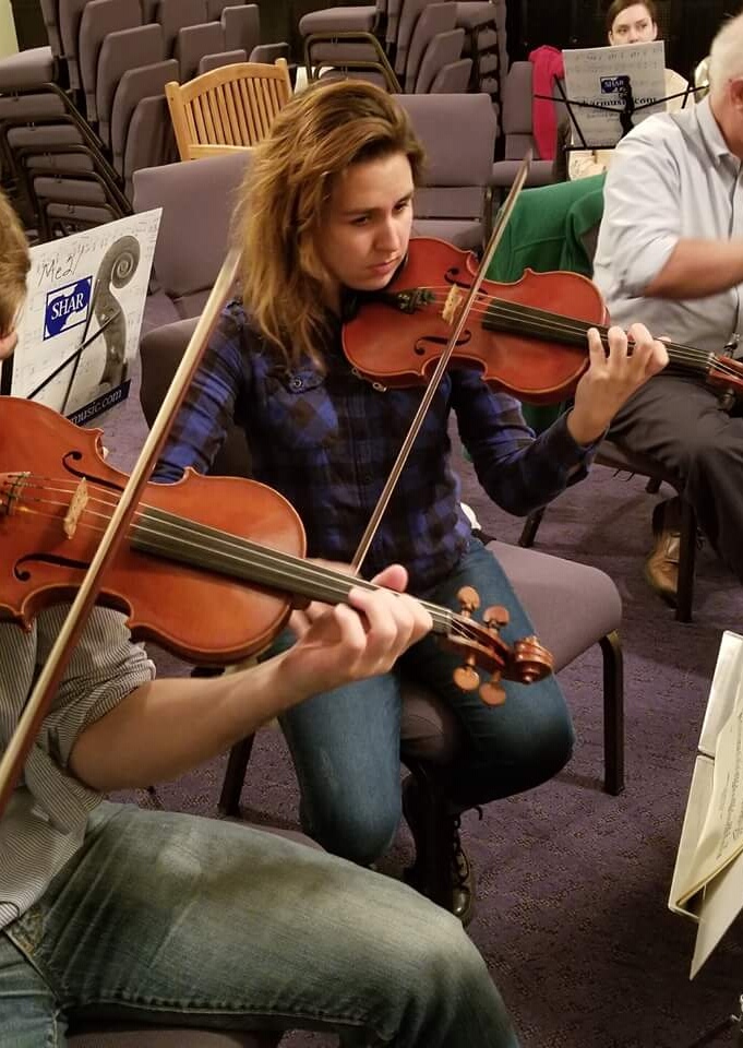 Woman seated playing the violin in an orchestra