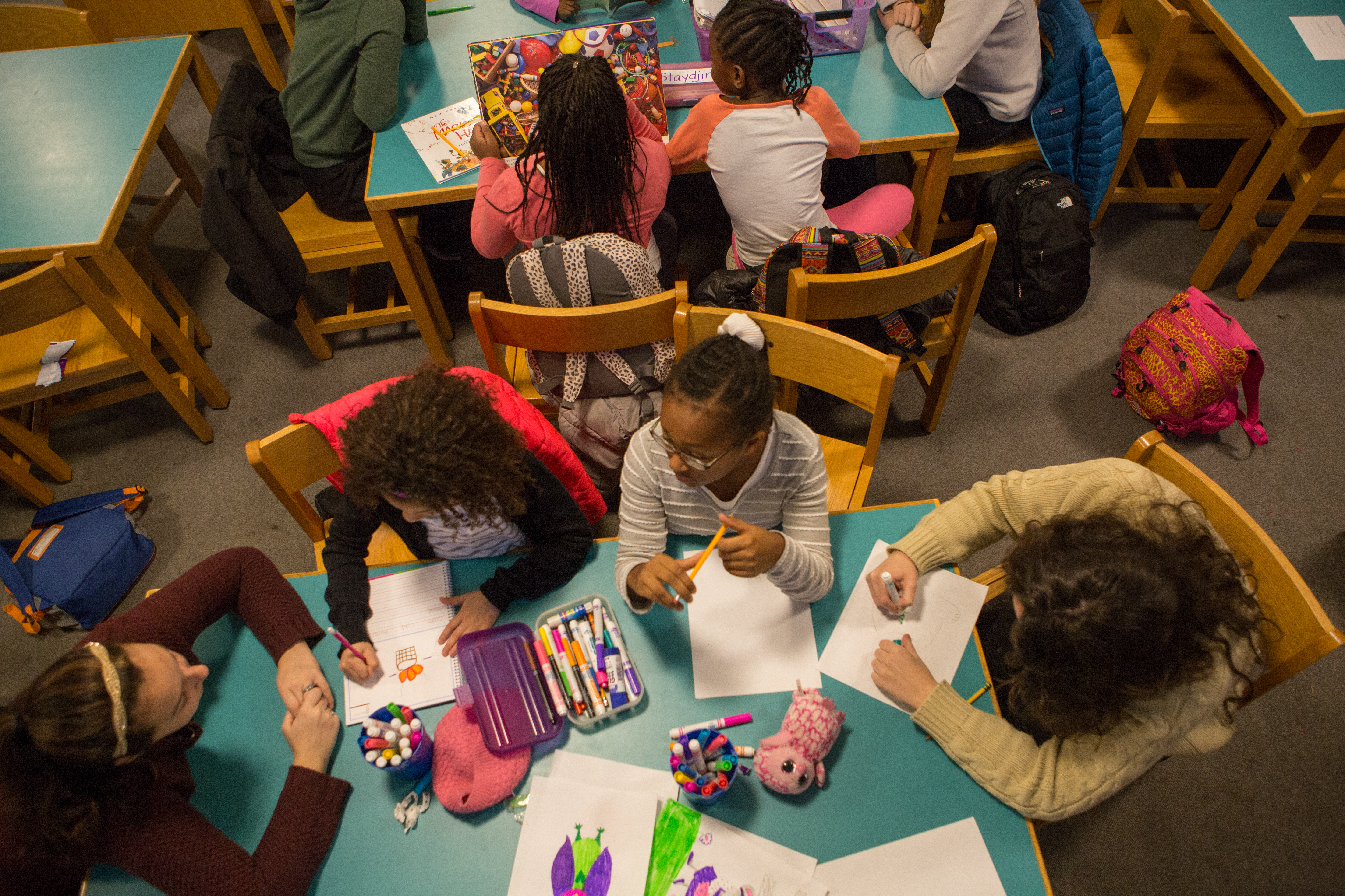 Tutors and students sitting at a table with books and markers and paper in a library 