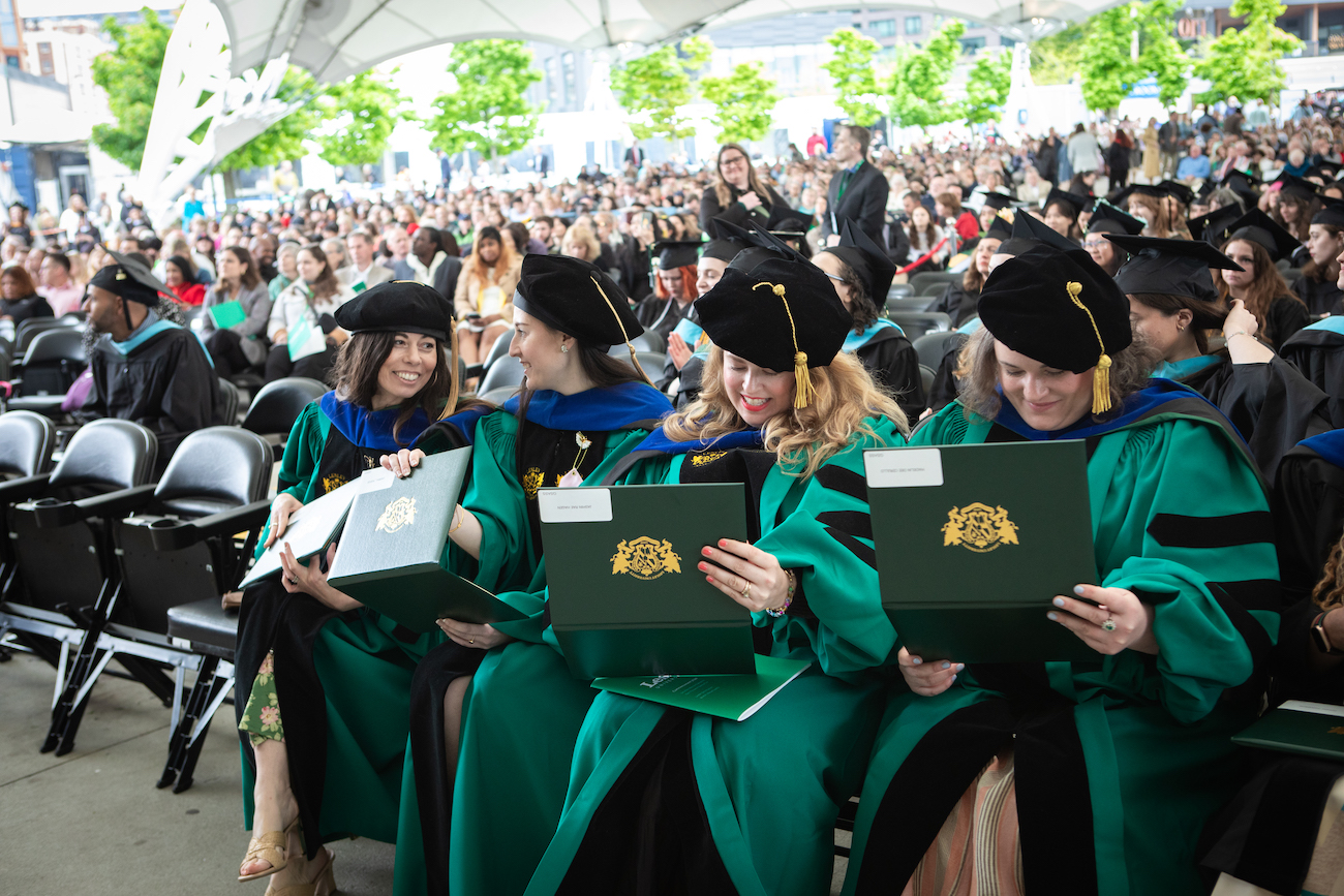 Graduates sitting in chairs holding diplomas smiling