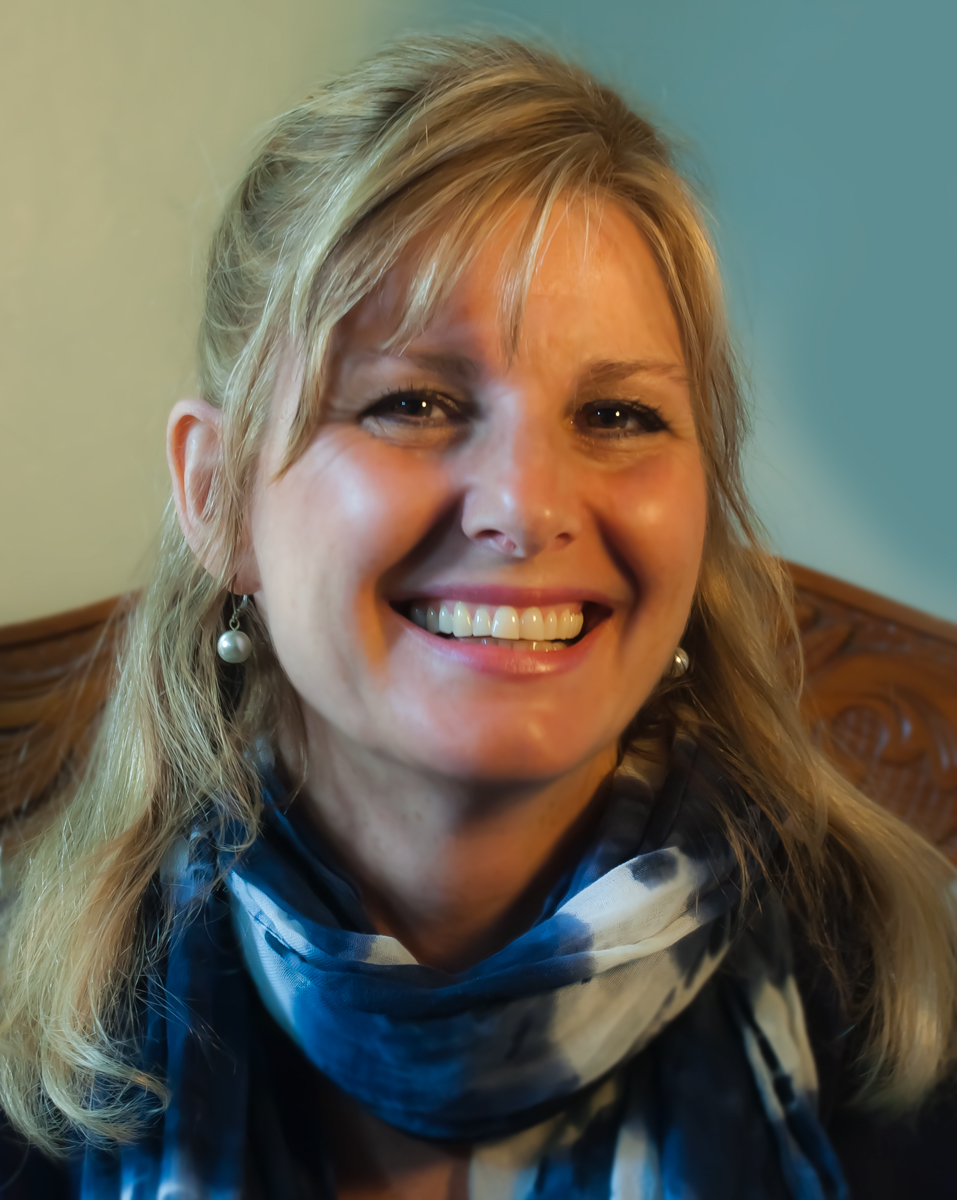 Headshot of woman smiling, with blonde hair and scarf around her neck