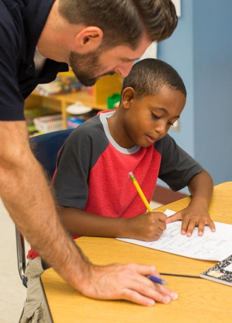 student practicing writing with a teacher's help