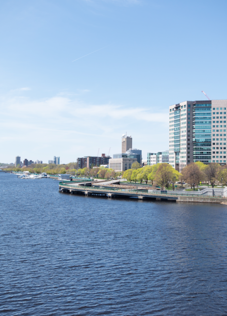 Photograph of the Charles River with blue sky and blue water and buildings of Cambridge in the background.