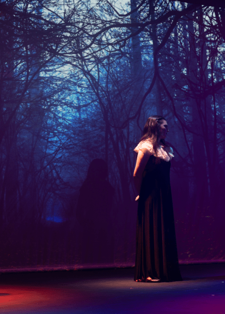 Three actors on stage against the backdrop of the woods in a production of Macbeth