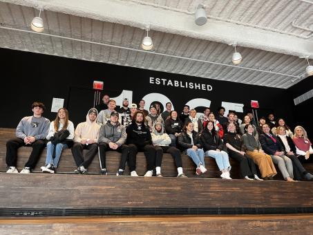 Students sitting on wooden bleachers smiling for a photo