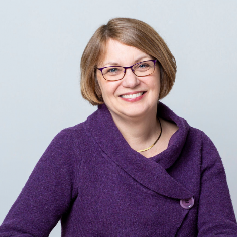 Headshot of Alison Angell. Alison has bobbed blonde hair, glasses, and wears a purple sweater. She smiles while looking at the camera. 