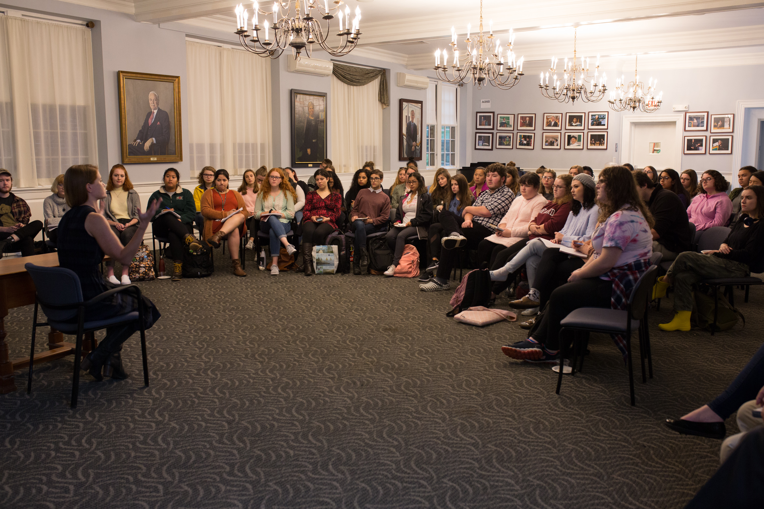 A women with long red hard sitting in a chair speaking to an audience of students